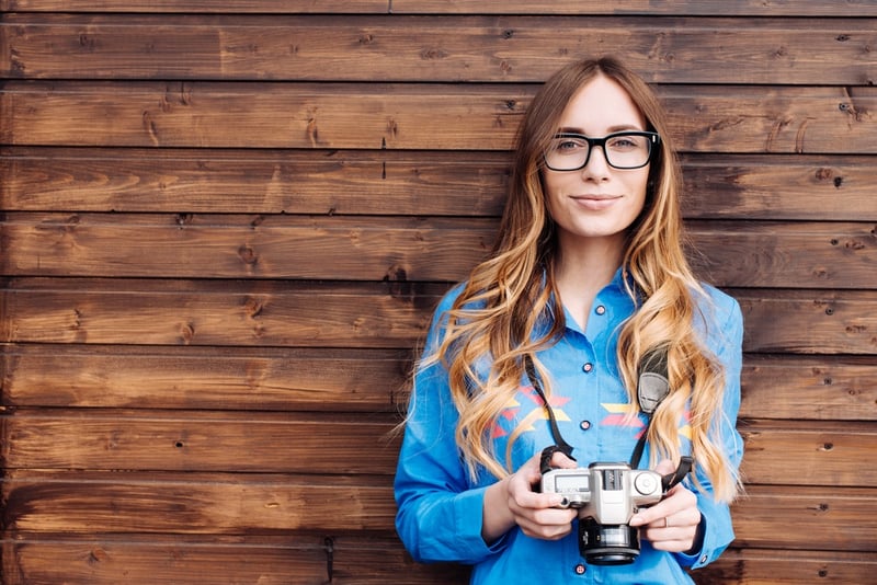 Happy young hipster woman in glasses holds retro photo camera